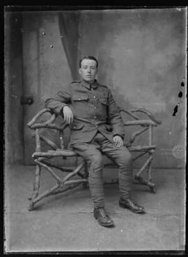 [Studio portrait of a soldier seated on a rustic bench]
